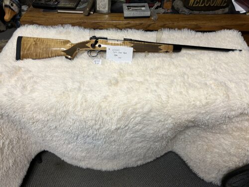 Custom wooden rifle displayed on white furry blanket.