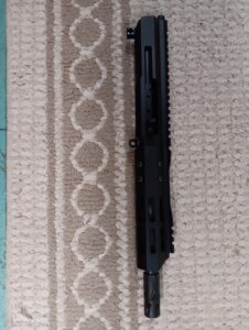 Black rifle upper receiver on beige patterned carpet.