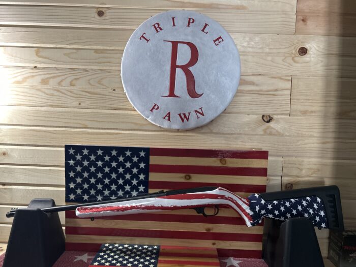 American flag-themed rifle displayed on wooden wall.