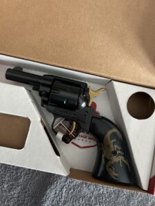 Black revolver with scorpion engraving in box.