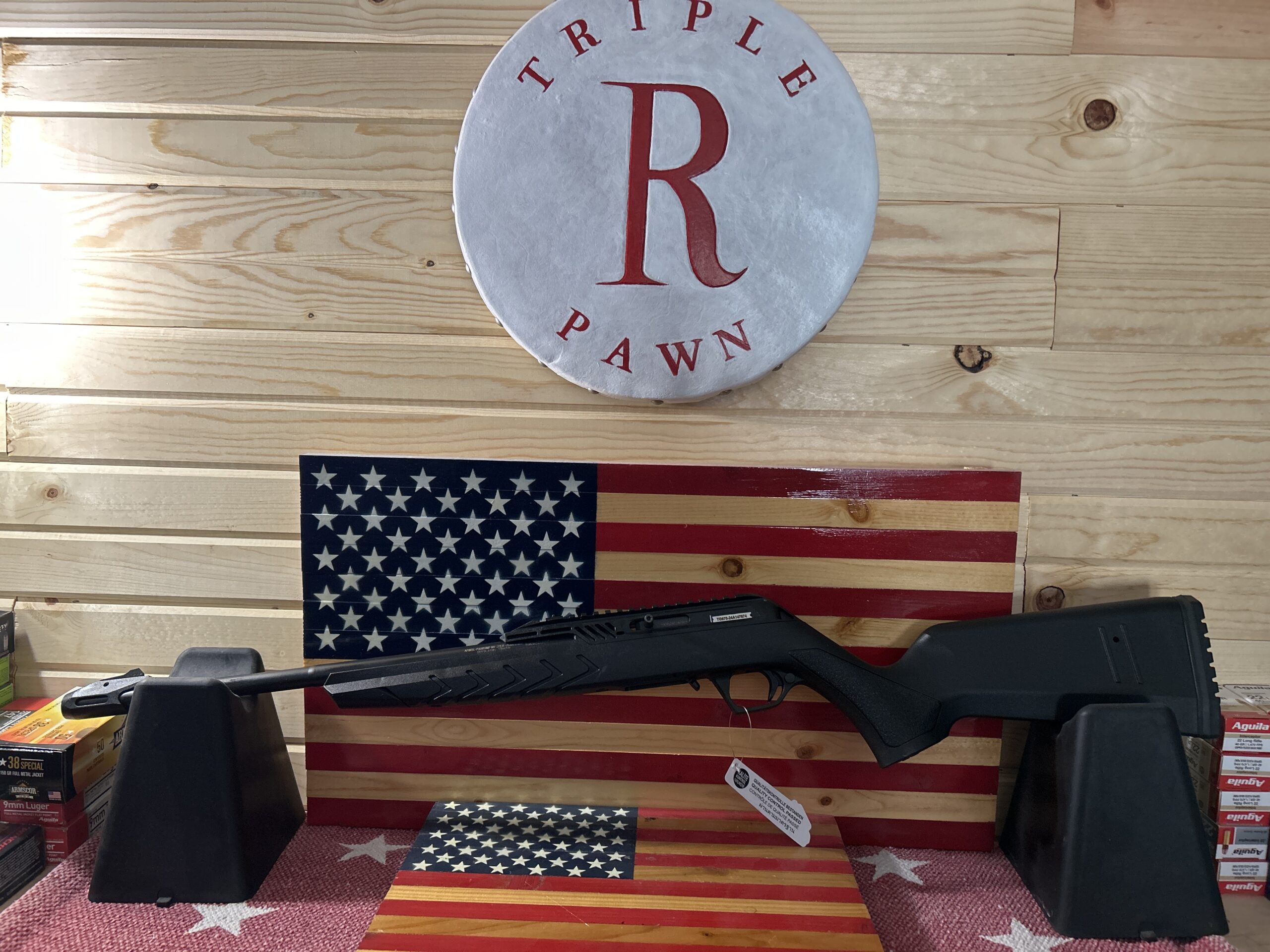 Rifle displayed with American flag backdrop in store.