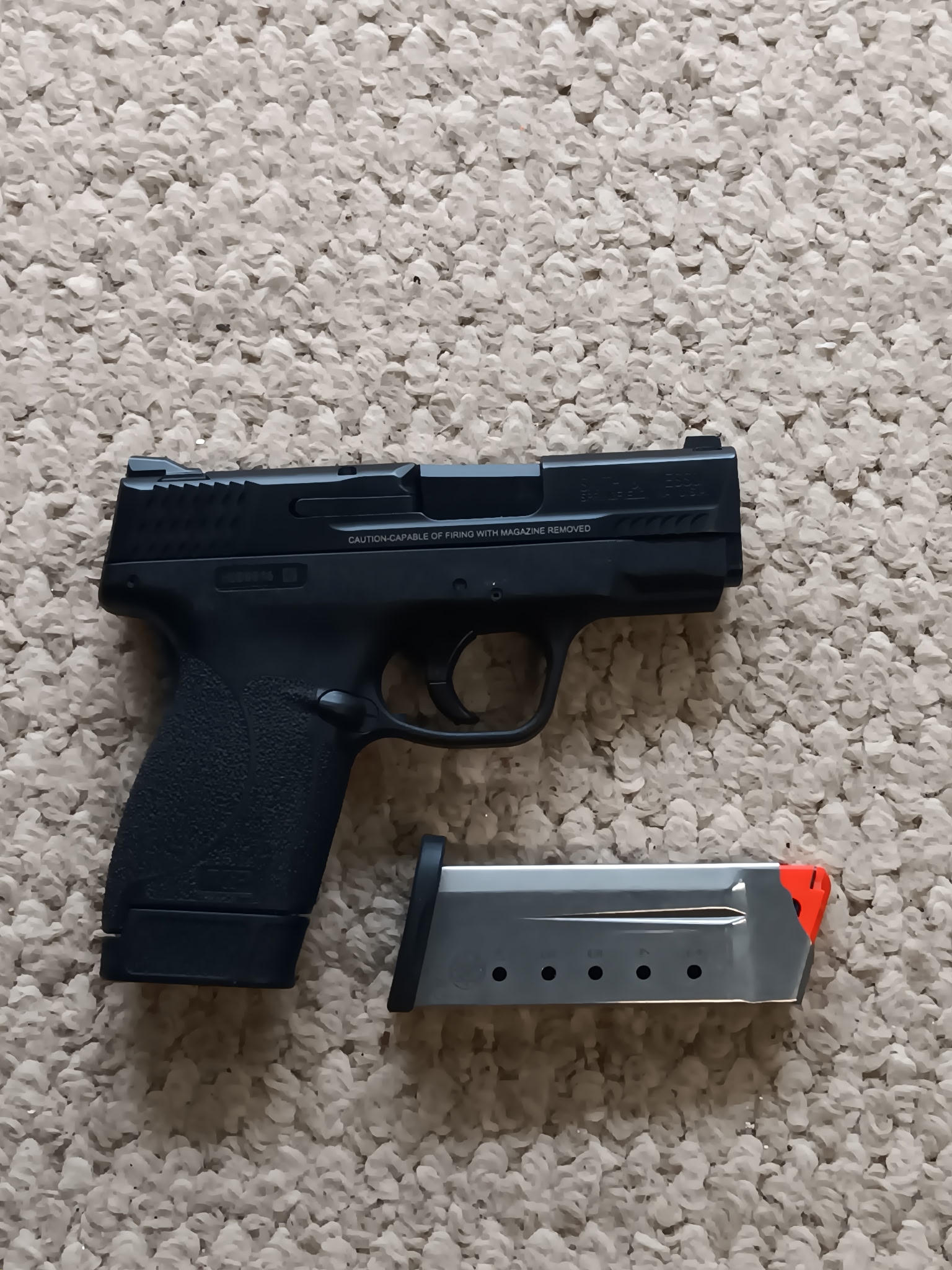 Black handgun with magazine on beige carpet.
