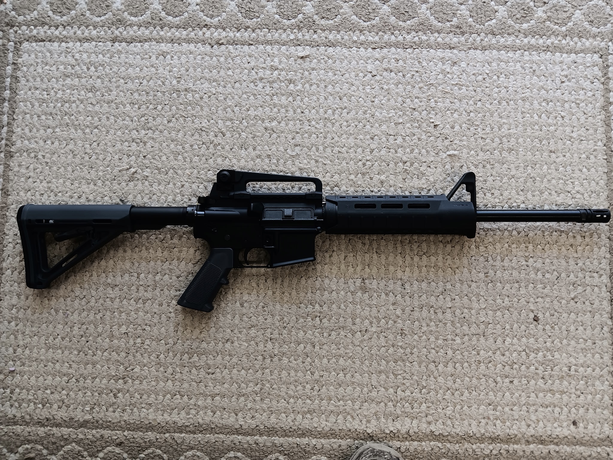 Black rifle on beige carpet surface.