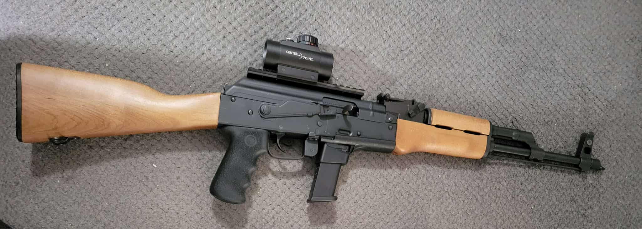 Semi-automatic rifle with wooden stock on carpet.