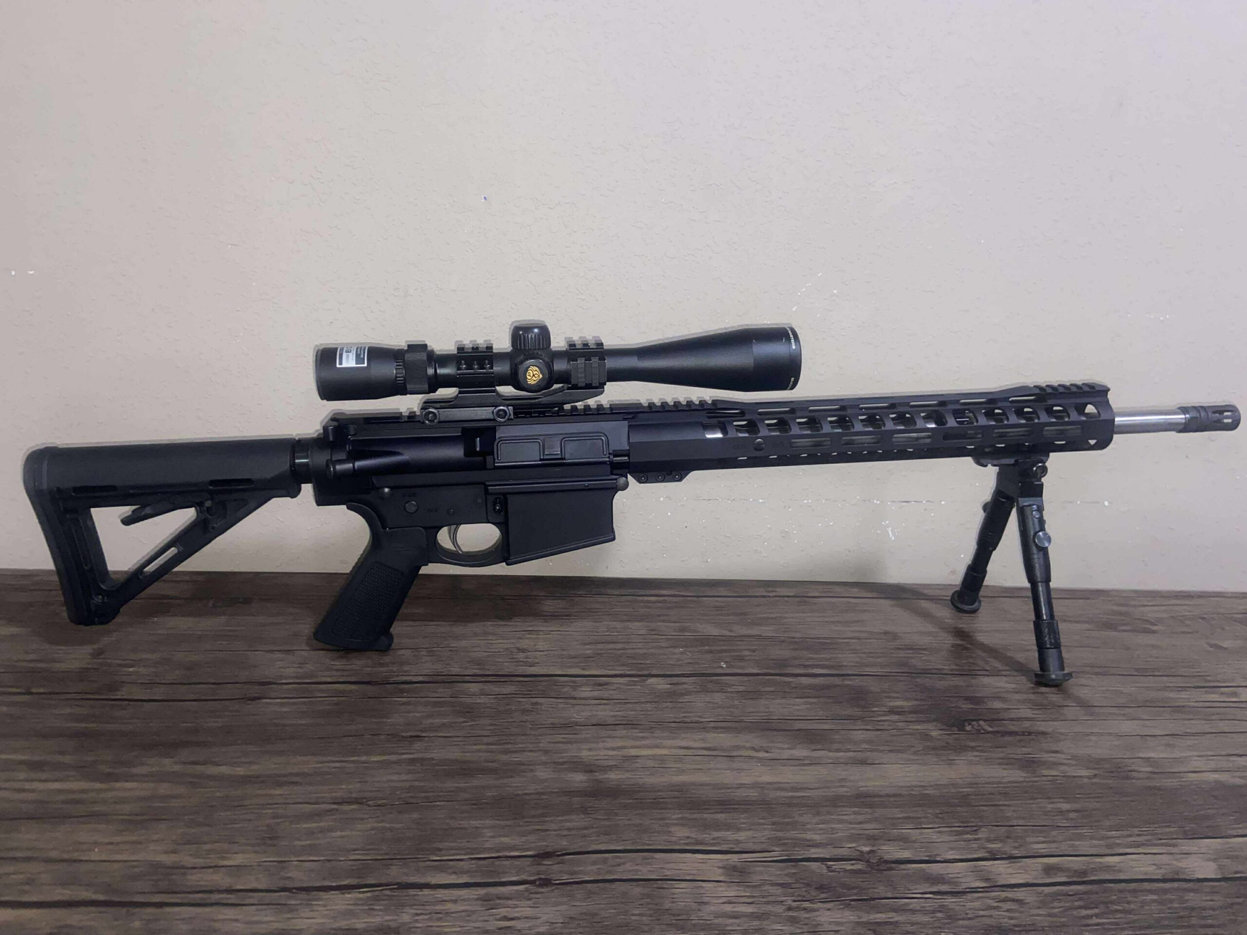 Tactical rifle with scope and bipod displayed on table.