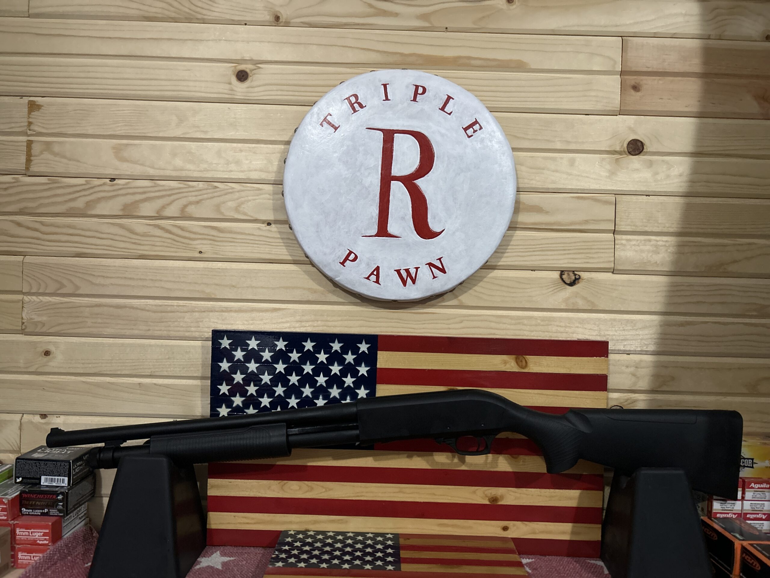 Shotgun displayed with American flag and store logo.